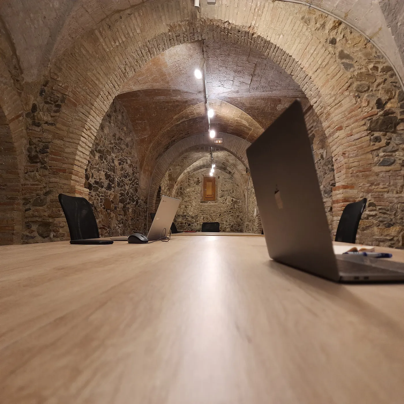 Interior del coworking Espai Pràctic amb la volta catalana de pedra i taules amb portàtils